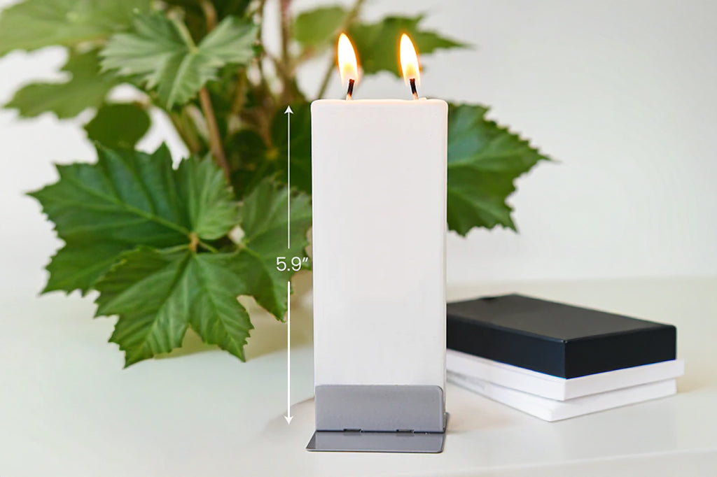 White candle with a steel holder base near a plant on a desk. Dimensions show it is 5.9"high
