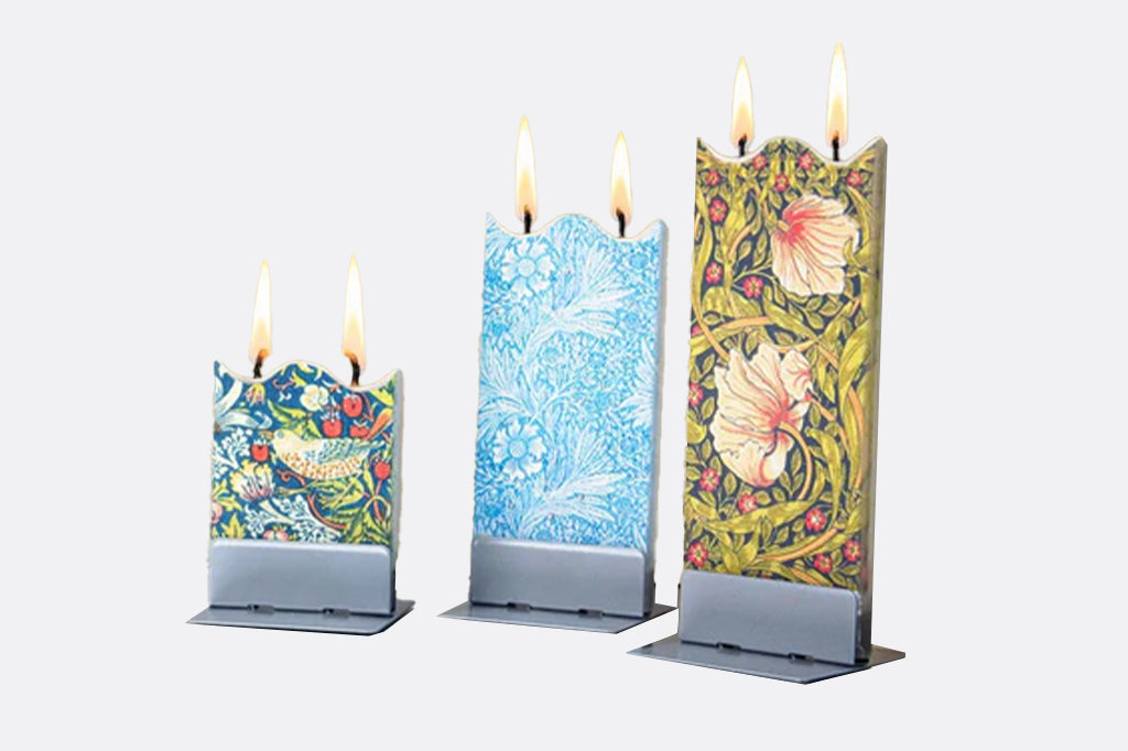 Three decorative candles with floral designs on a white background - they each have two wicks and they all are at different heights after burning for several hours.