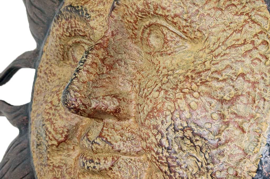 close up detail of sculpted dimpling on cast metal sun wall plaque with face