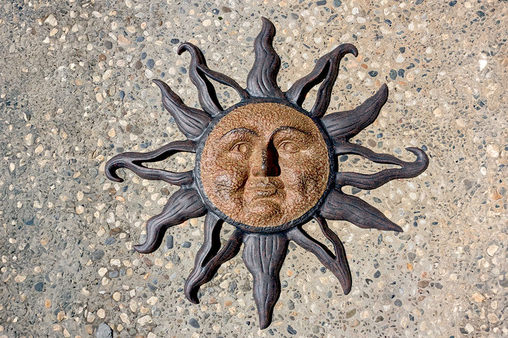 cast metal sun wall plaque with face shown hanging on stone wall