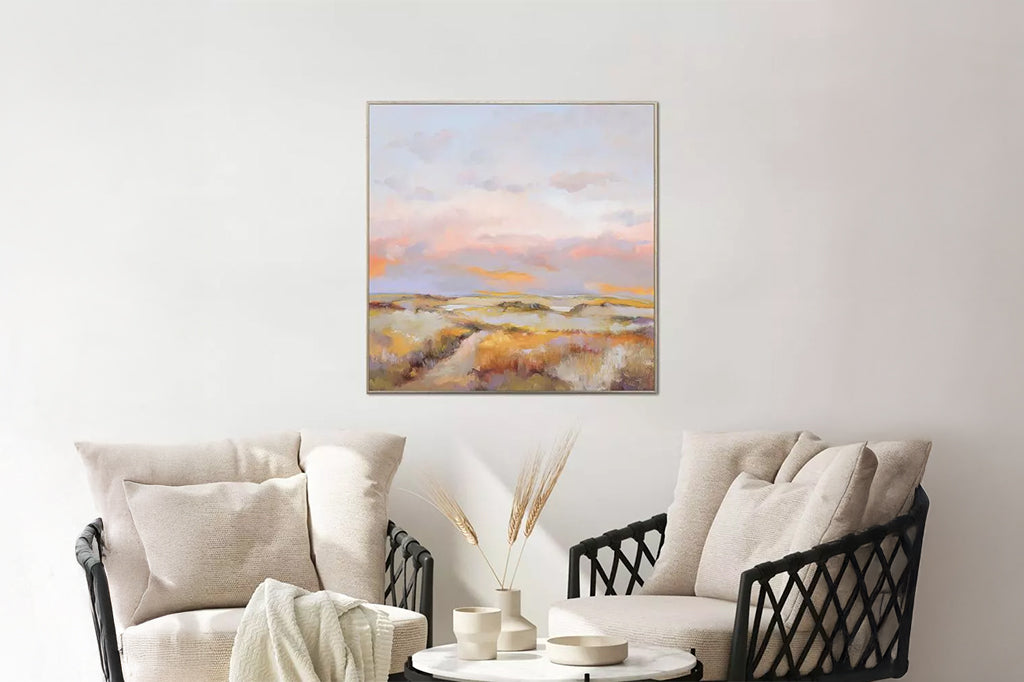framed art of soft pink orange sunset over nature on wall behind a seating area