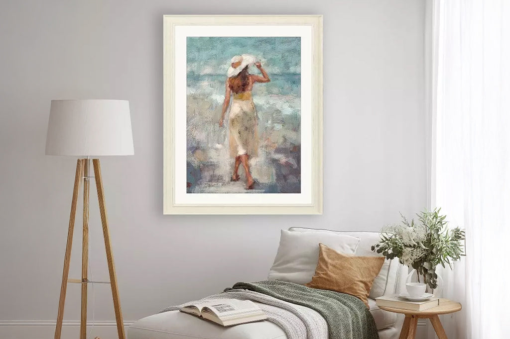 An impressionistic beach scene captures a graceful woman walking along the beach. Matted in buff and framed in a distressed ivory wood. Mounted on wall above day bed