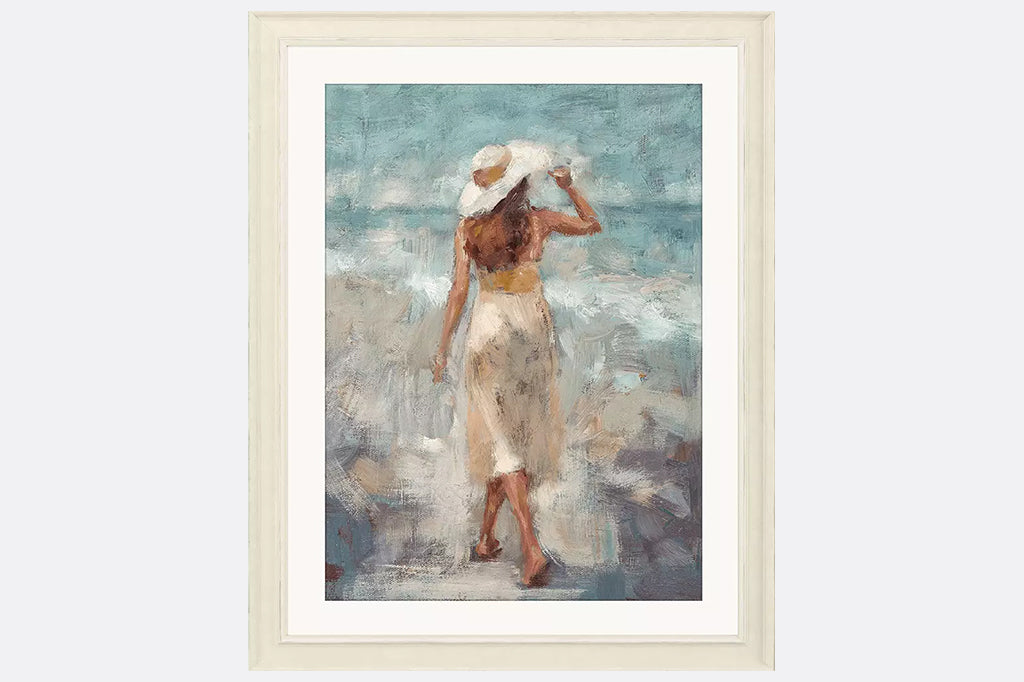 An impressionistic beach scene captures a graceful woman walking along the beach. Matted in buff and framed in a distressed ivory wood.