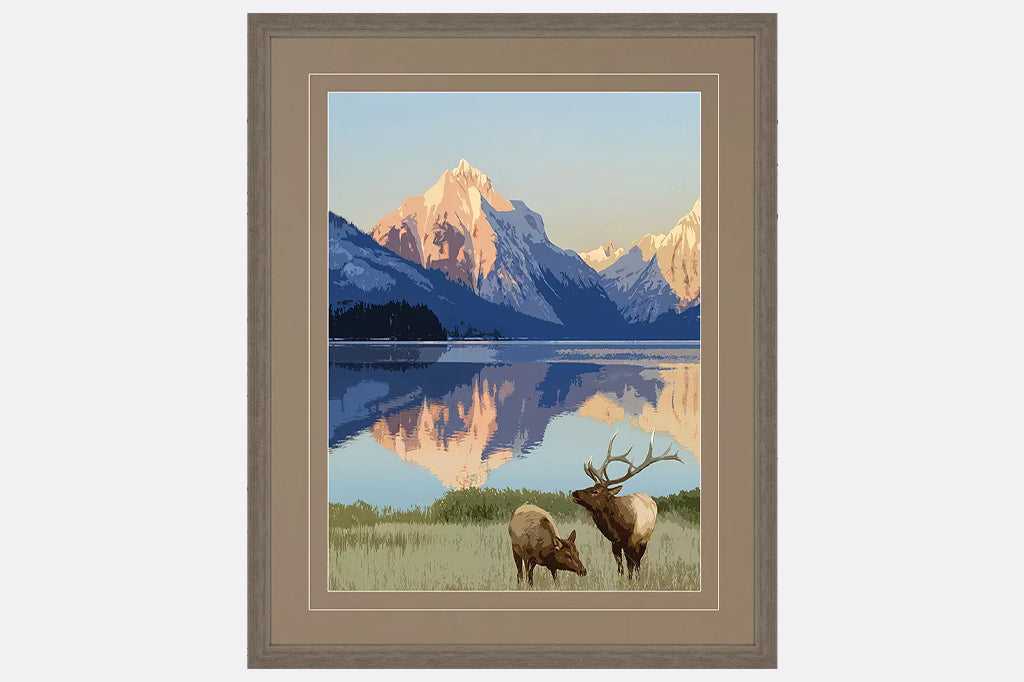 Framed artwork of a mountain range and lake with two moose