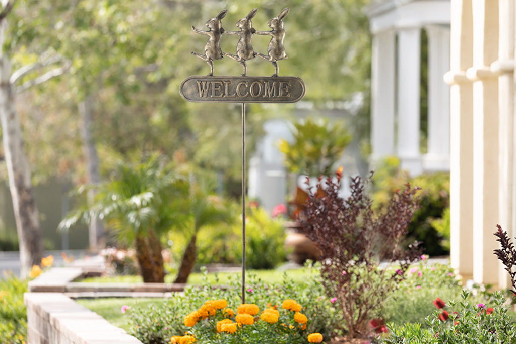 Trio of dancing rabbits decorate a metal staked welcome garden sign near a front walkway of house