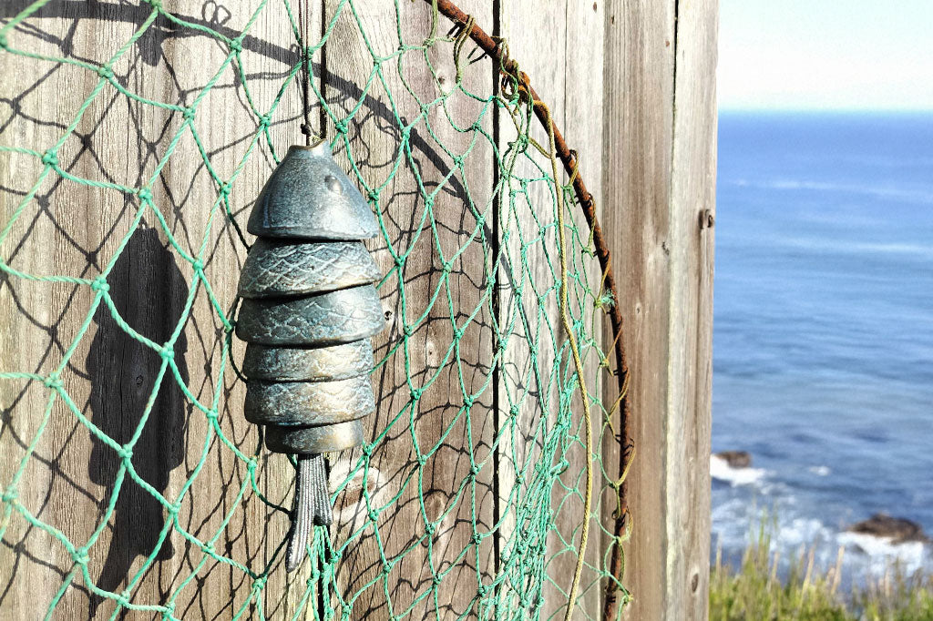 cast metal sculpted hanging art of fish with 7 parts that clang when moved, shown on crab net on weathered fence by the ocean