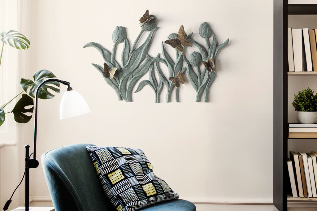Decorative wall art with butterflies on tulips on a white wall above a chair with a patterned pillow.