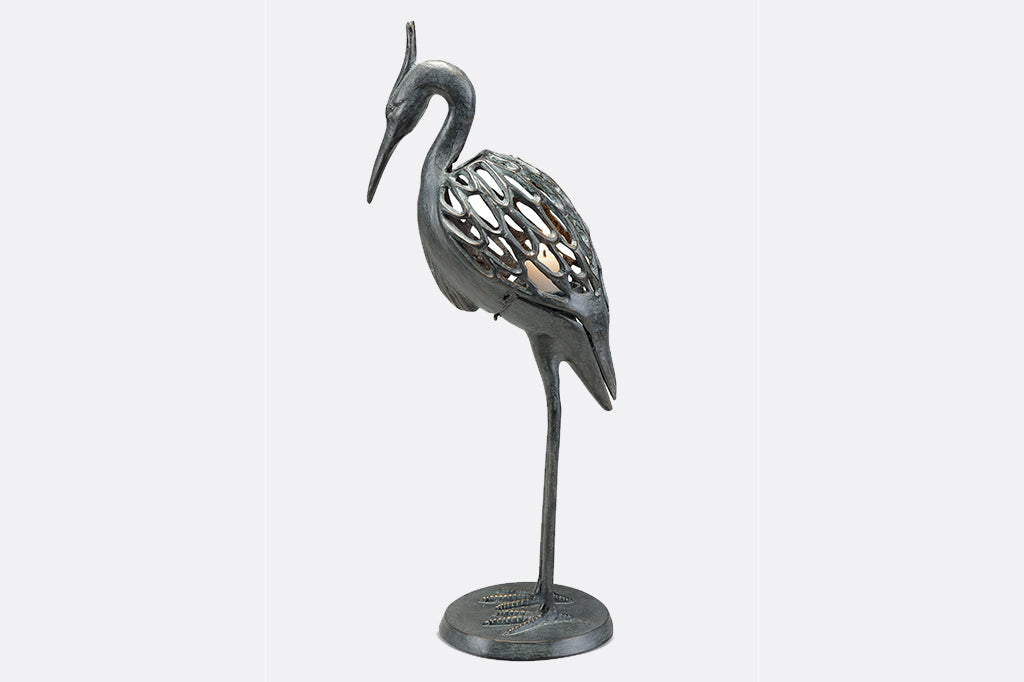 Modern metal heron candleholder with white lit candle face left