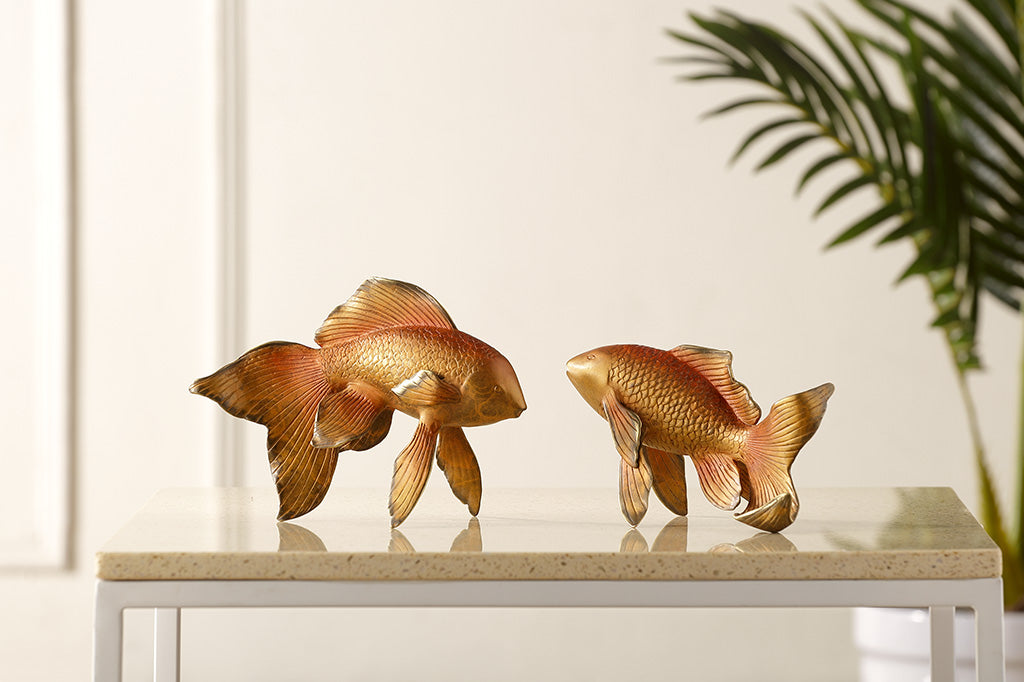 Two gold fish sculptures on a marble surface with a plant in the background