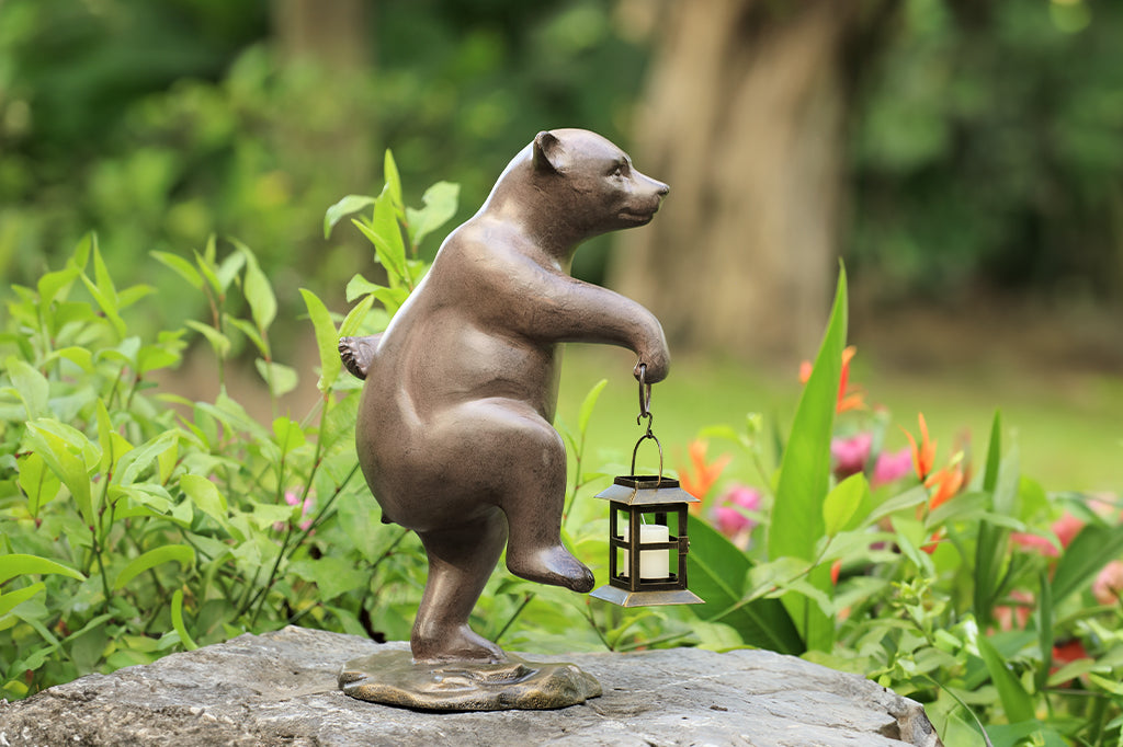 cast metal sculpture of bear walking holding a lantern in hand