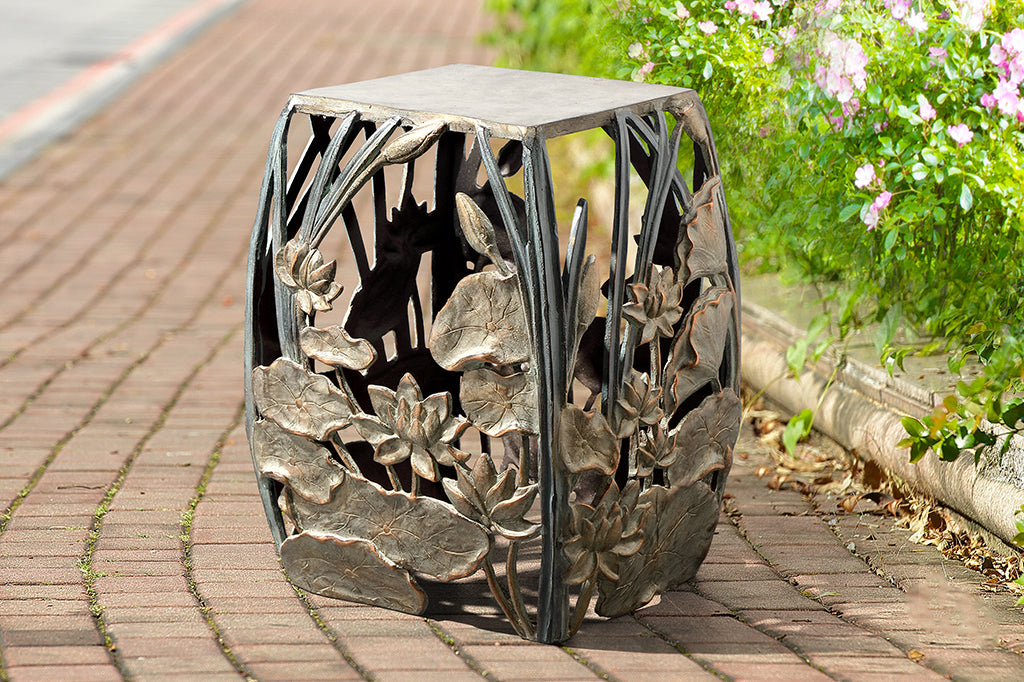 cast metal lotus flowers and cattails squared garden stool, floral design on all four panels of stool. Shown on brick pathway next to flower bed