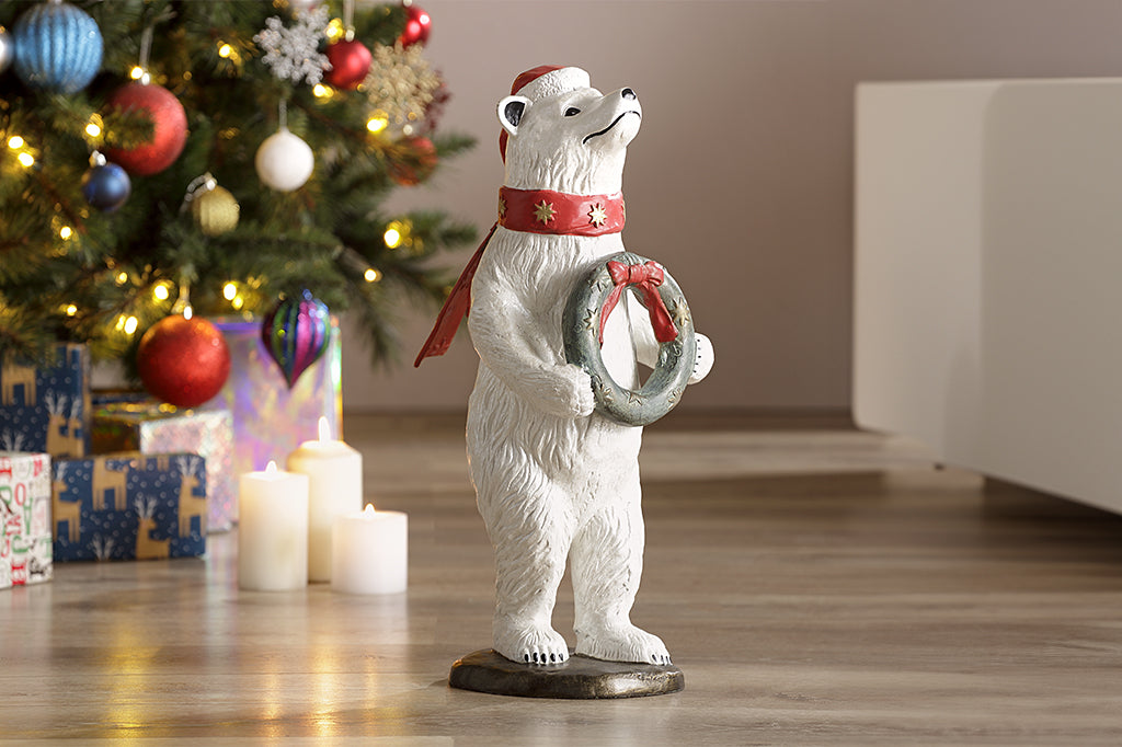 cast metal polar bear sculpture with star scarf holding a wreath under Christmas tree
