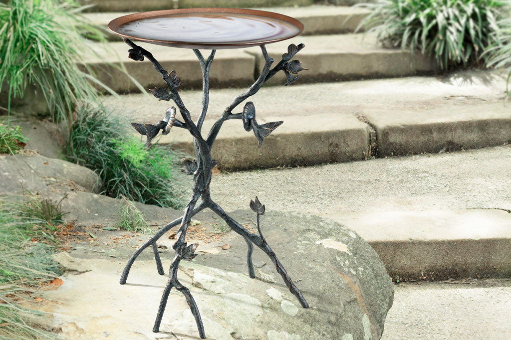 Water shown in the basin of the Hummingbird and Flowers Birdbath with sculpted metal birds and blossoms is in a rock garden