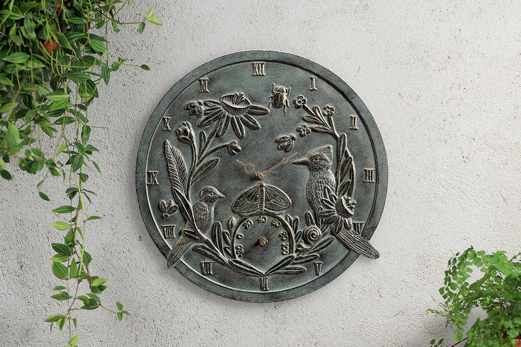 Outdoor sculpted clock & thermometer featuring birds, bugs, and blossoms; shown on concrete wall with hanging plants
