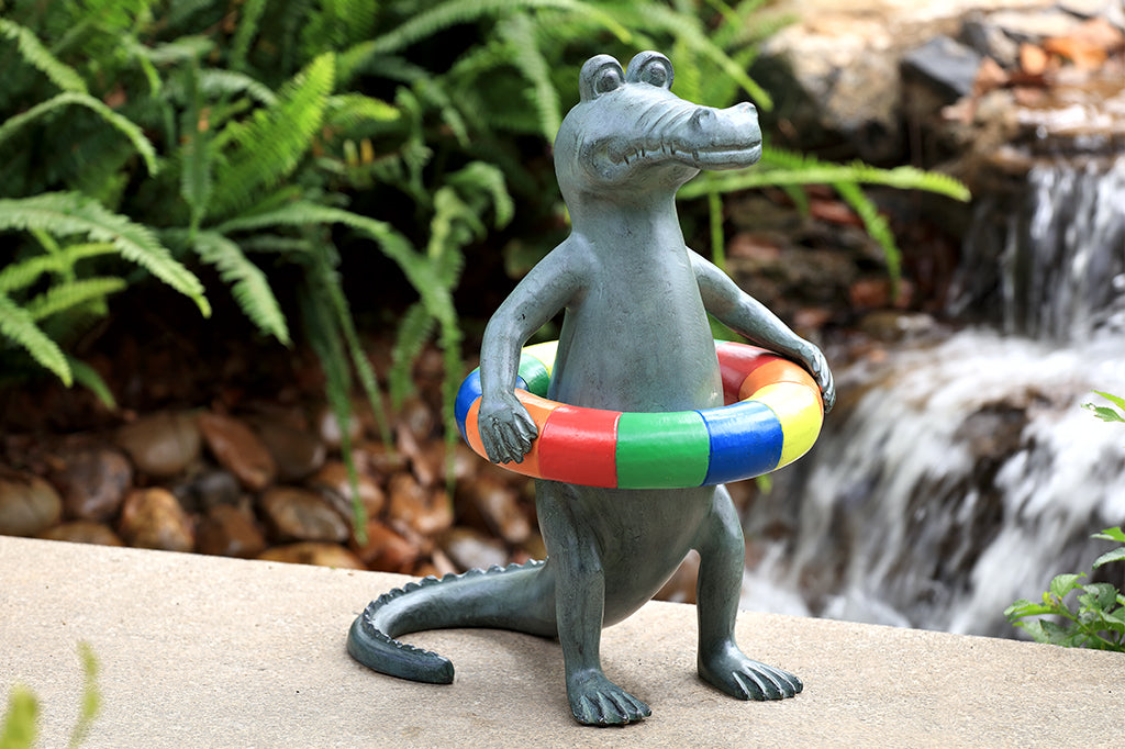 Alligator garden sculpture with primary colored innertube around body placed in garden waterfall scene 