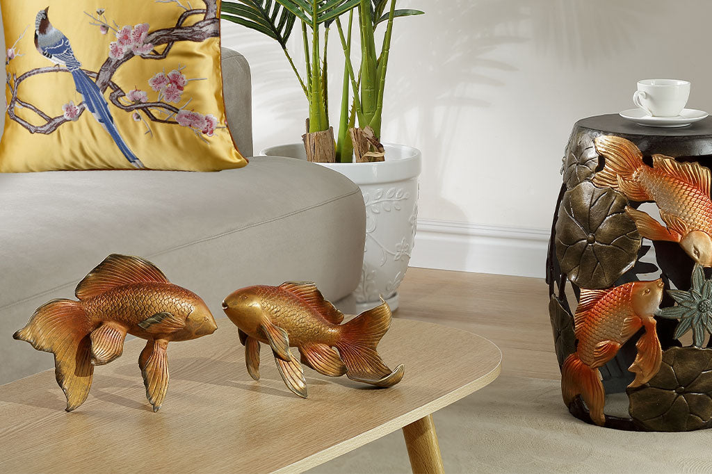 Decorative goldfish on a table with a pillow and plant in the background