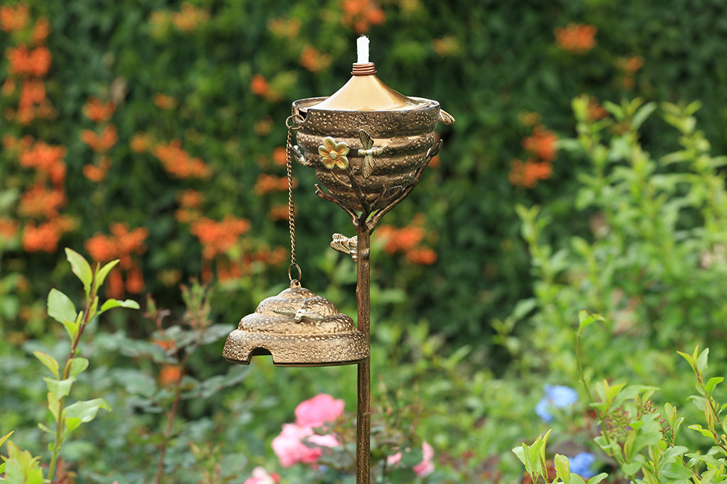 Metal Beehive oil torch with cap on, flower and small bee details. Cap off placed in garden