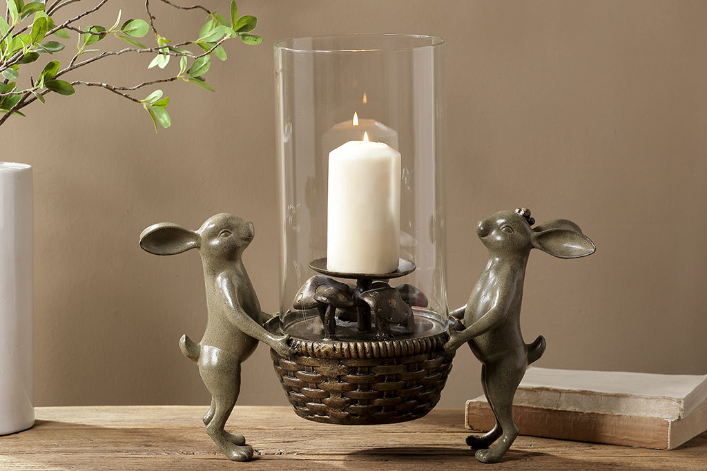 Cast metal bunnies holding a basket candleholder. Small mushroom detail under candle.