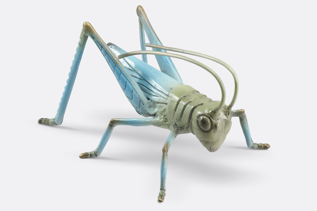 cast metal garden sculpture of grasshopper, shows hues of soft blue and sage green