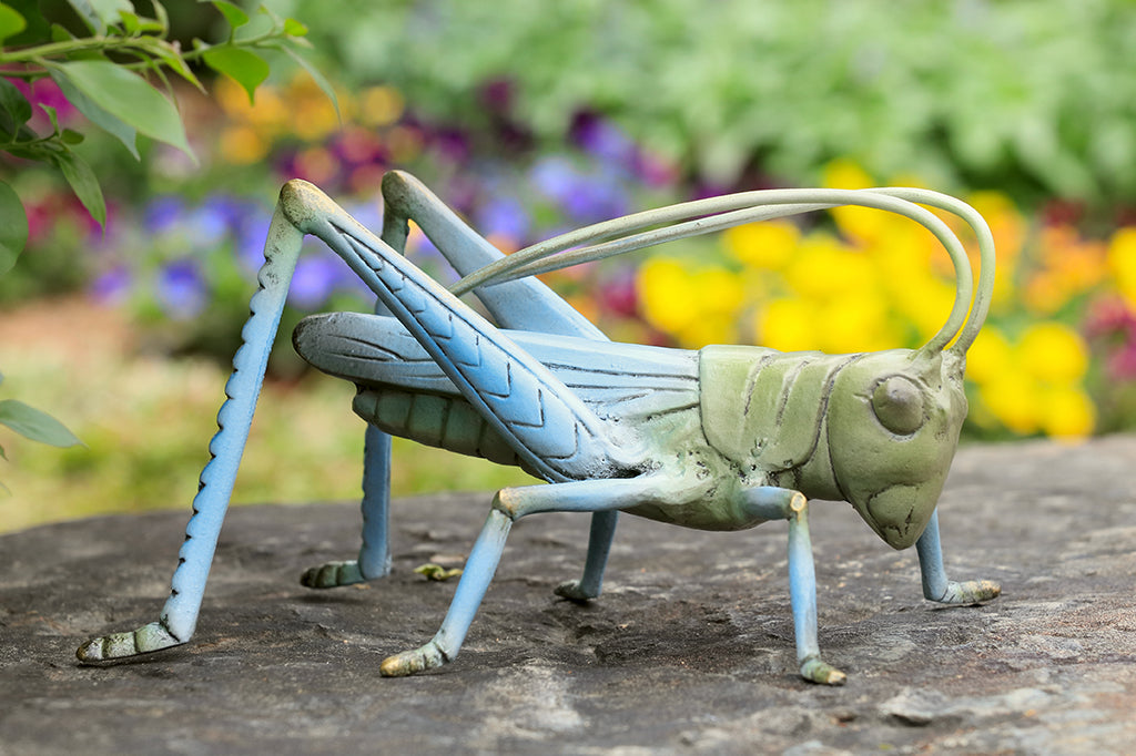 cast metal garden sculpture of grasshopper, shown in flower garden