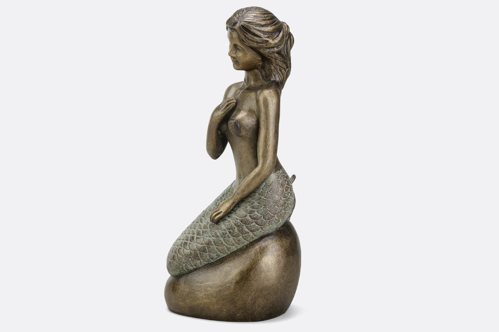 Metal mermaid seated on a rock garden sculpture face left 