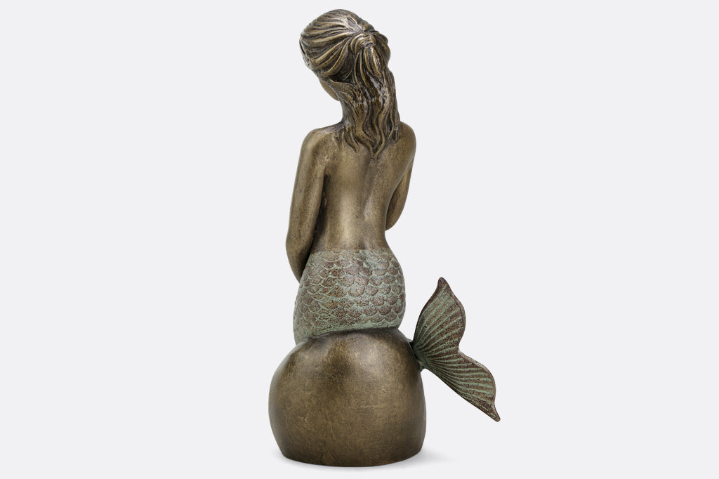 Metal mermaid seated on a rock garden sculpture face back 