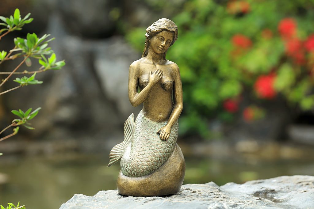 Metal mermaid seated on a rock garden sculpture staged outdoors 