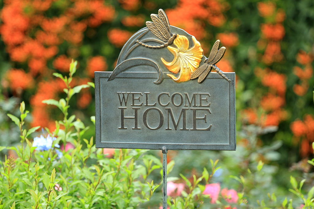 Metal dragonfly and lily welcome home sign, staged against flower bed 