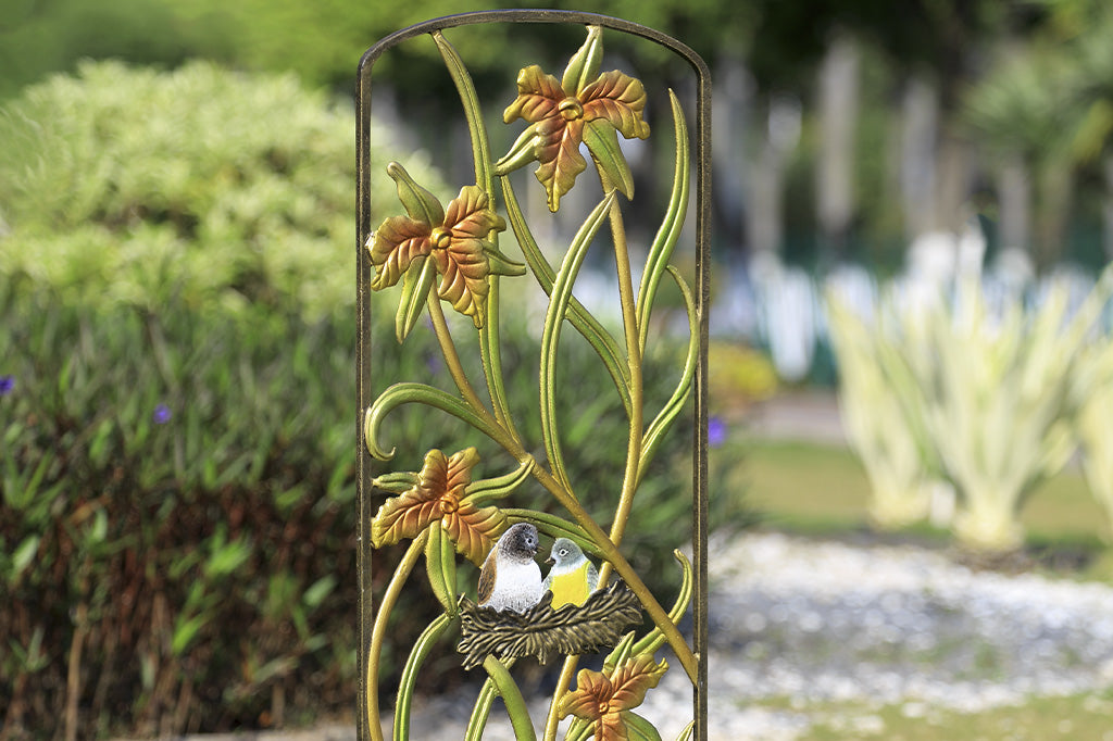 Amongst The Lilies Garden Trellis in a garden. features shimmery pastel finish and a nest with 2 birds