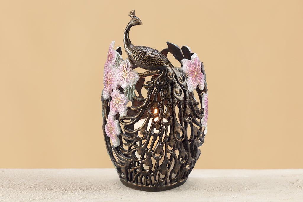cast metal candleholder with peacock feathers and blossoms holding white pillar candle