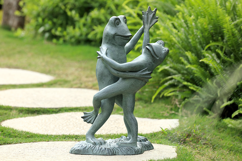 cast metal dancing frog sculpture one frog tipping the other over in a tango. Placed in green garden, full of ferns