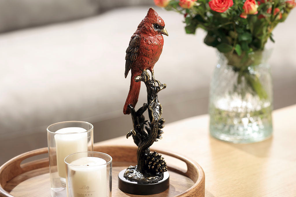 Brass sculpture of cardinal on branch, shown on coffee table by flowers and candles