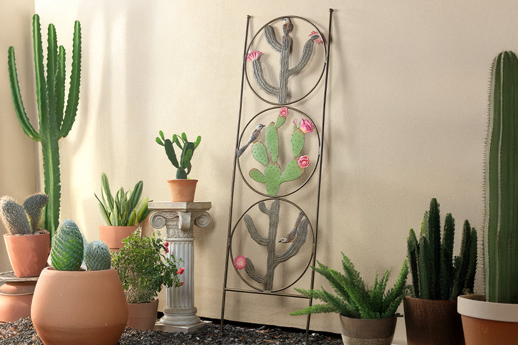 cast metal trellis with circles and cacti motifs with birds as design leaning against wall surrounded by potted cacti