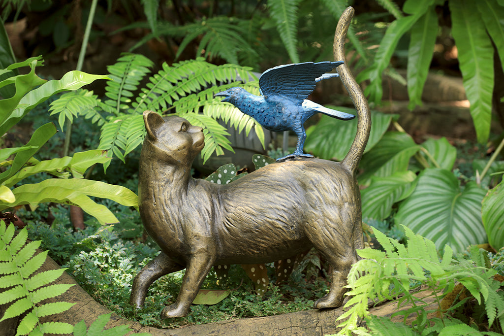A garden sculpture featuring a metallic cat with a blue pumpkin-like flower on its back, with a smaller cat figurine on top.