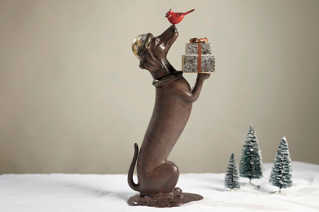 Hello, Friend Garden Sculpture features a Dachshund sculpture holding wrapped gifts while a red cardinal perches on its nose.