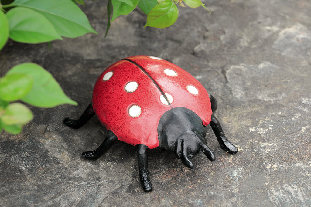 red lady bug cast metal garden sculpture shown in gray rock