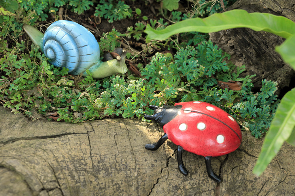 speckled red lady bug garden sculpture with blue snail set in shade garden scene