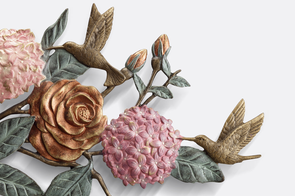 detail view of cast metal plaque. rose buds, hummingbirds fluttering near pink hydrangea blooms