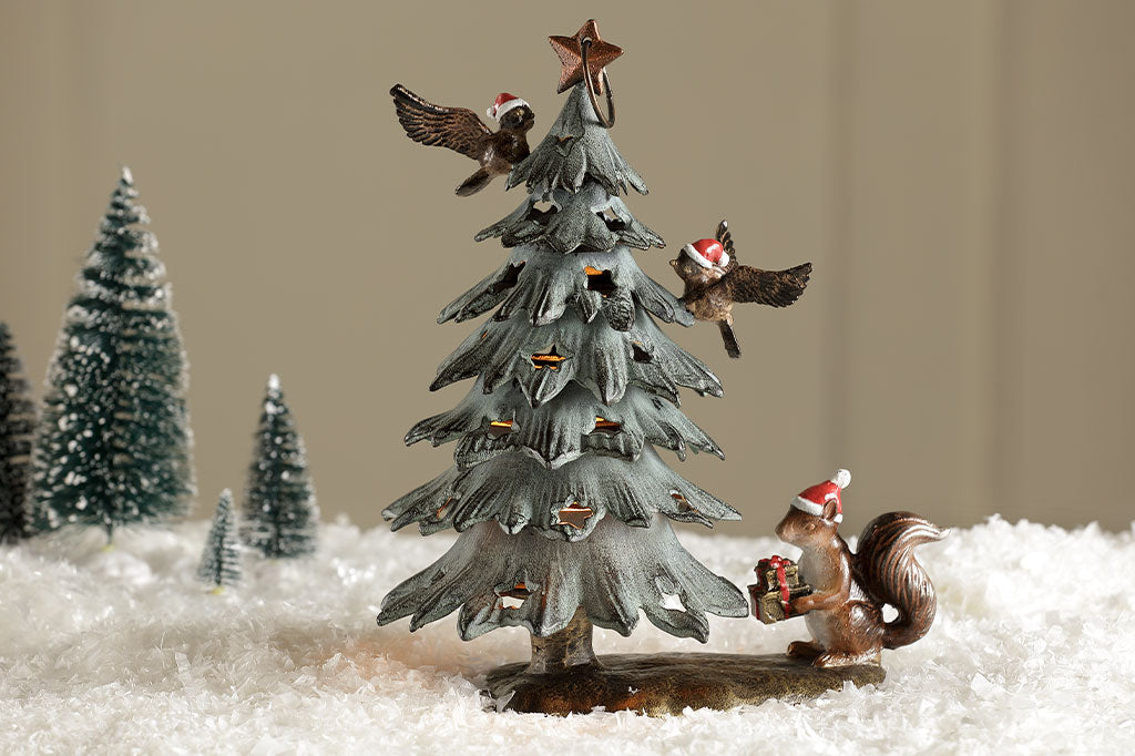Cast metal christmas tree lantern with birds and squirrel in santa hats shown on table with faux snow and bristle christmas trees