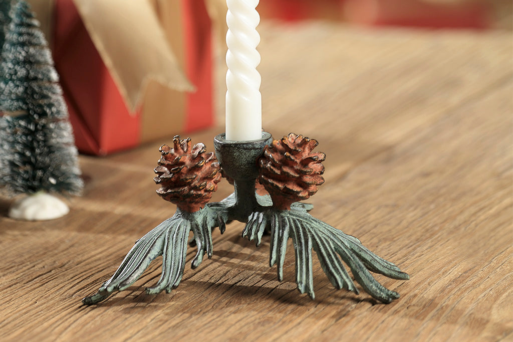 taper candle holder shaped like pineneedle cluster with 3 pinecones shown on table by bristle trees and wrapped present