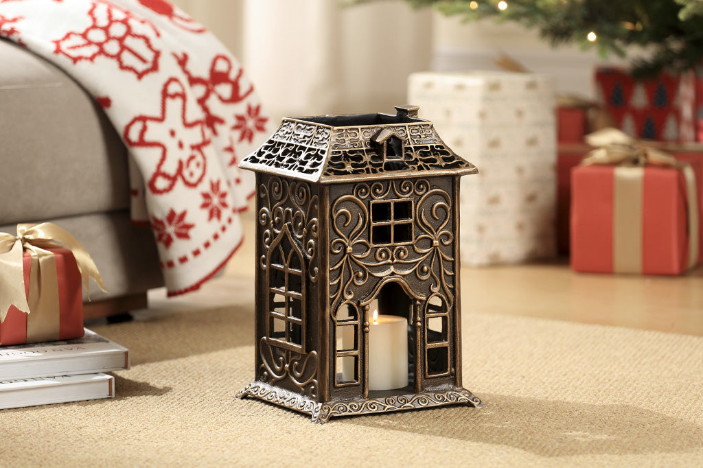 Cast metal house candleholder styled with Victorian style "gingerbread" embellishments like scrollwork and arched window fretwork - shown on living room rug with Christmas decor in background