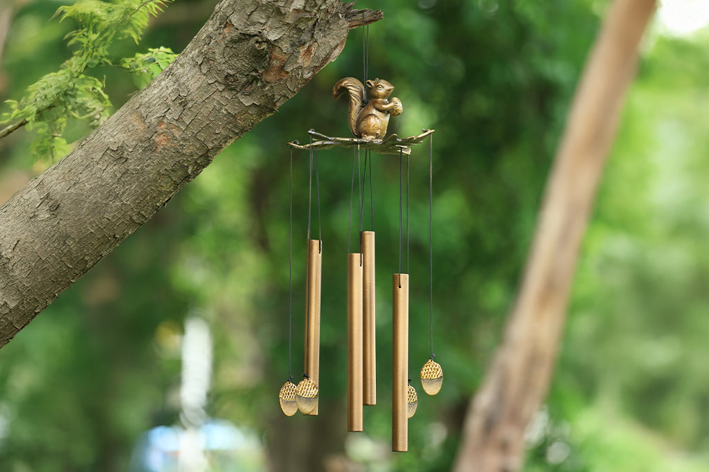 cast metal squirrel holding an acorn windchime set on tree outdoors