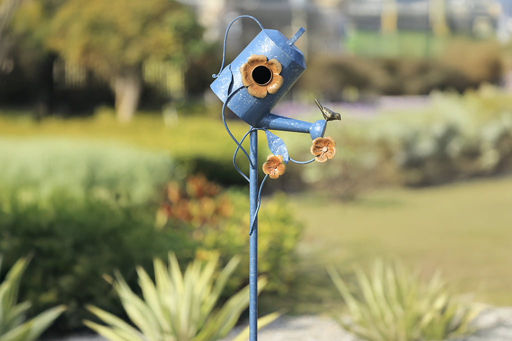 Blue sheet metal watering can with flowers birdhouse placed in garden