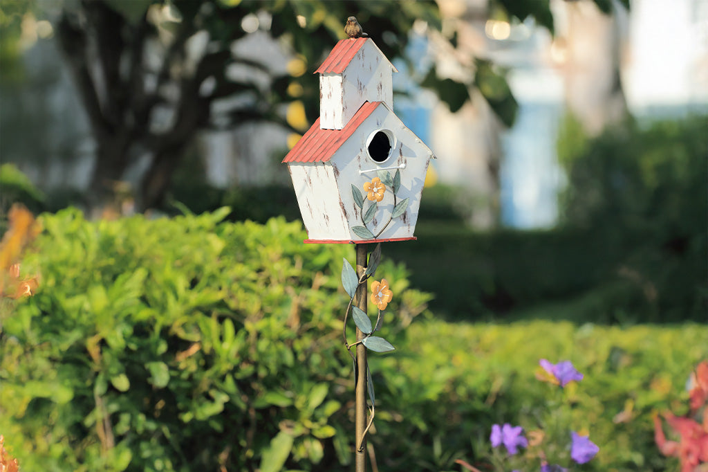 Decorative Iron birdhouse on stake, looks like rustic barn, accented with vining flowers and bird on roof