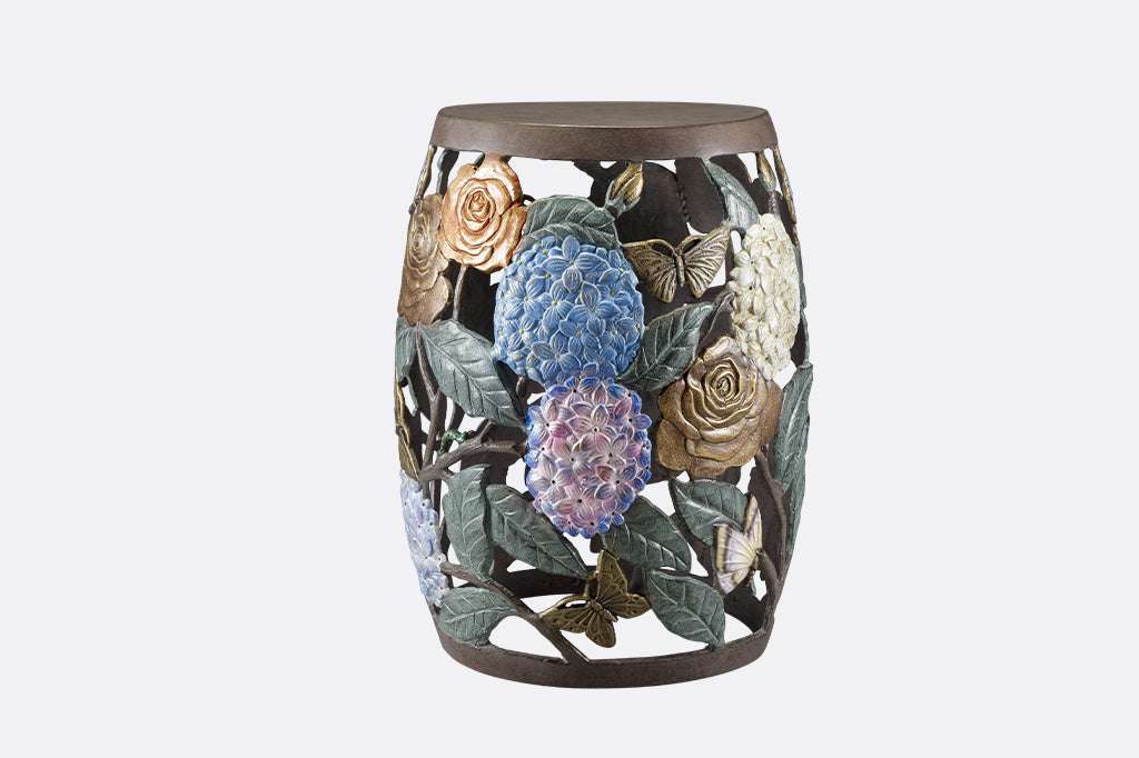 Cast metal garden stool features beautiful roses, butterflies, and the vibrant hues of hydrangeas.