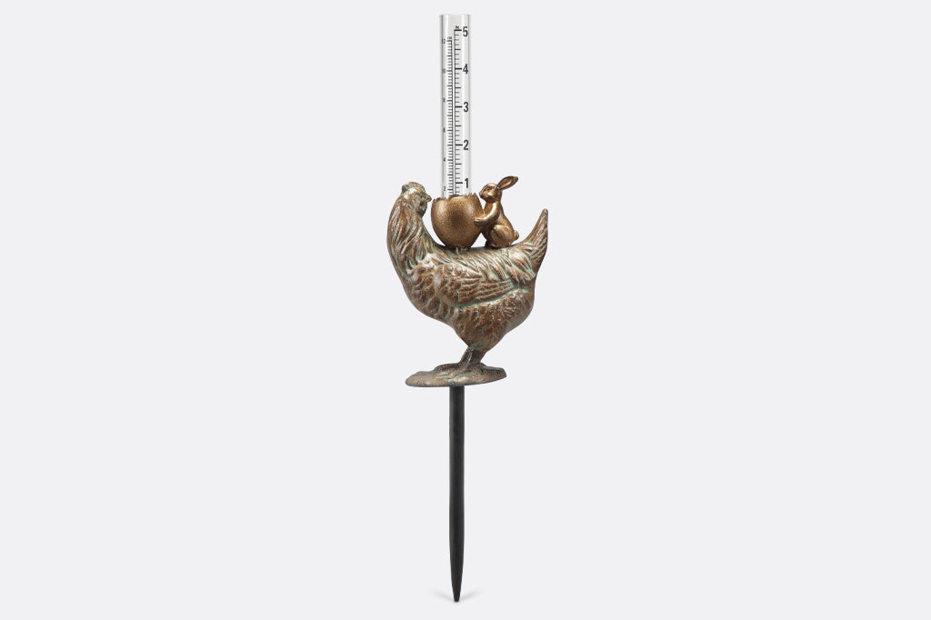 cast metal chicken with bunny holding a cracked egg holding a glass rain gauge face back
