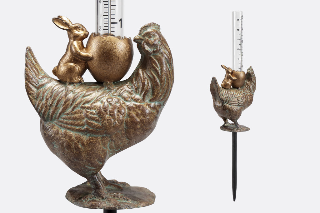 cast metal chicken with bunny holding a cracked egg holding a glass rain gauge