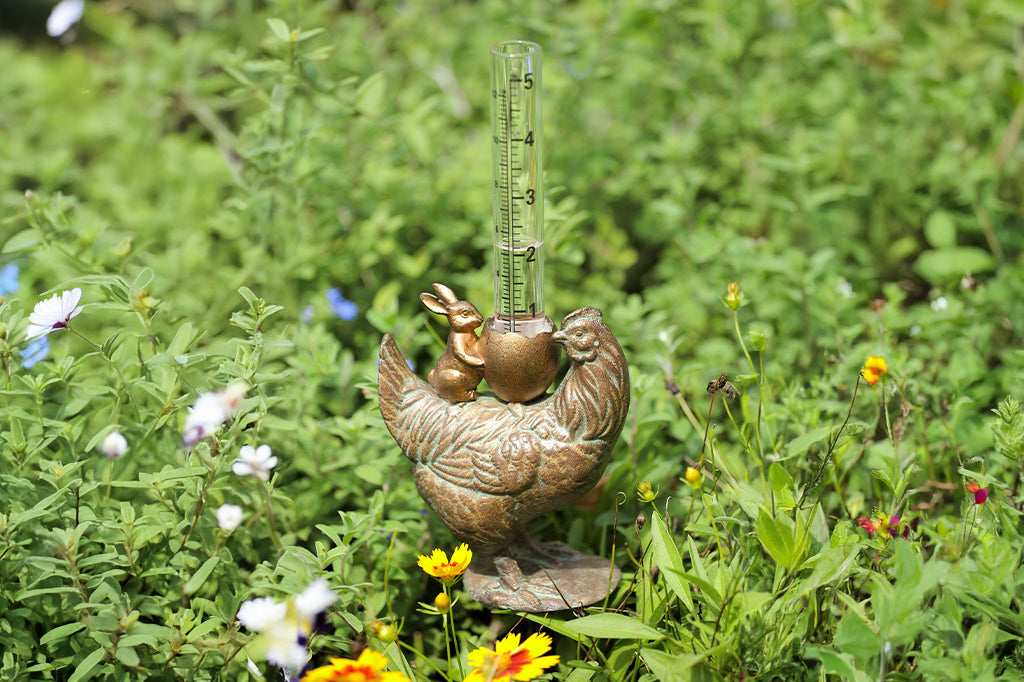 cast metal chicken with bunny holding a cracked egg holding a glass rain gauge set in garden