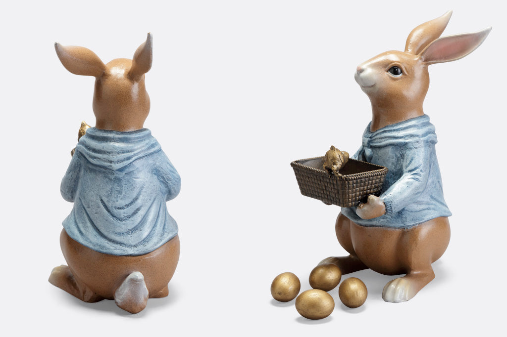 side view of cast metal sculpture of storybook-style rabbit in a blue shirt, holding a basket of four removable golden eggs. A chick perches on edge of basket to get a closer look. View shows eggs on floor in front of rabbit. Another view shows back side of bunny.