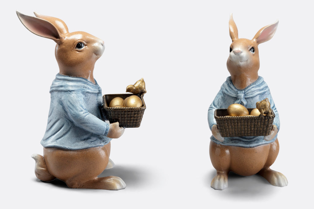 side view of cast metal sculpture of storybook-style rabbit in a blue shirt, holding a basket of four removable golden eggs. A chick perches on edge of basket to get a closer look.